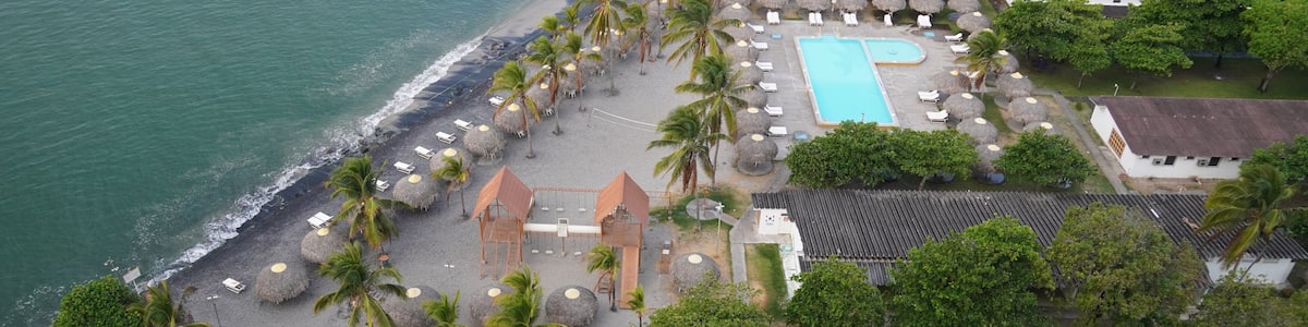 A resort with a swimming pool, beach, palm trees, and a view of the ocean.