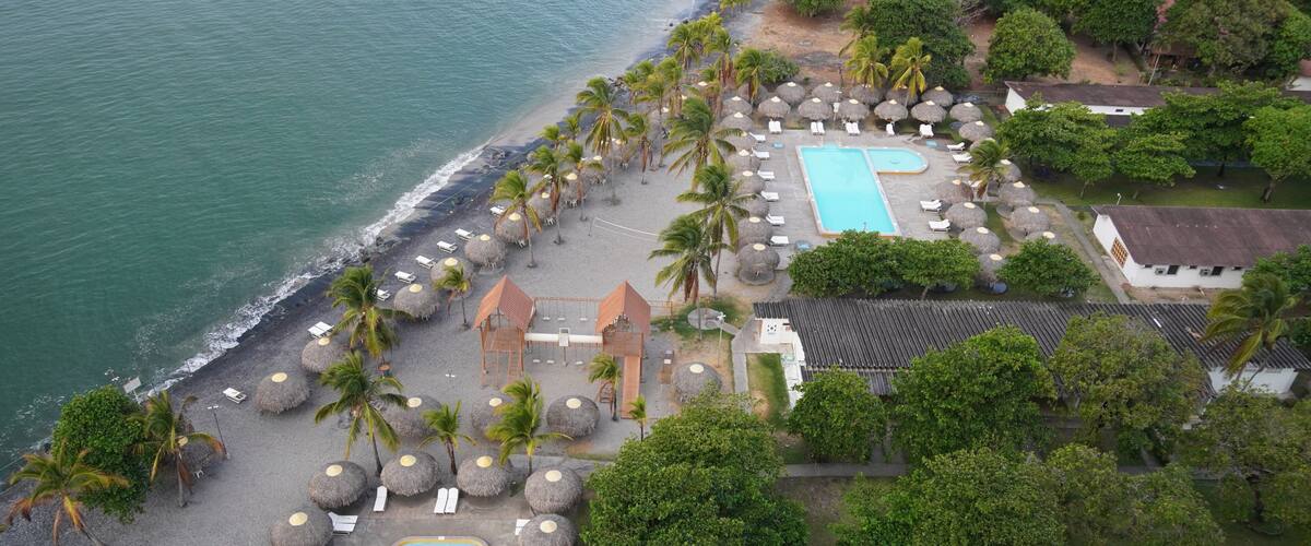 A resort with a swimming pool, beach, palm trees, and a view of the ocean.