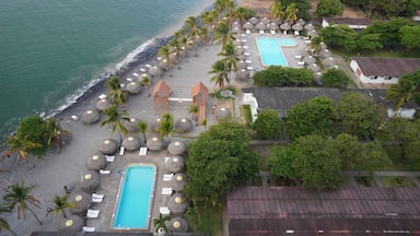 A resort with a swimming pool, beach, palm trees, and a view of the ocean.