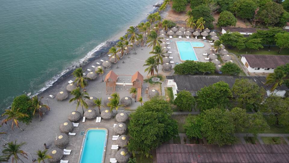 A resort with a swimming pool, beach, palm trees, and a view of the ocean.