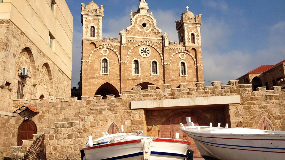 A historic church with two towers and a clock, surrounded by stone walls and boats.