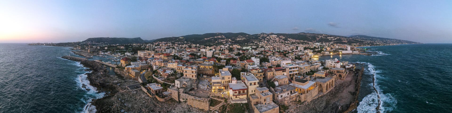 Panoramic sunset view of Batroun, Lebanon, showcasing the coastal city's blend of ancient walls, modern buildings, and picturesque shoreline along the Mediterranean Sea