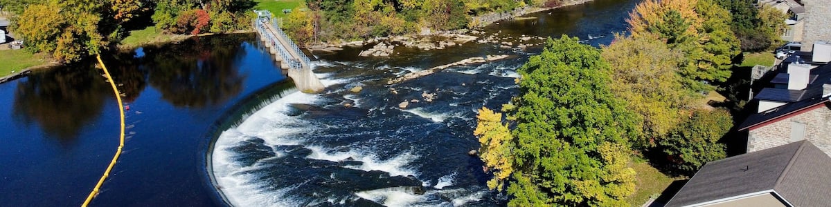 Ein Fluss mit einem Stausee, umgeben von herbstlich gefärbten Bäumen und Häusern.