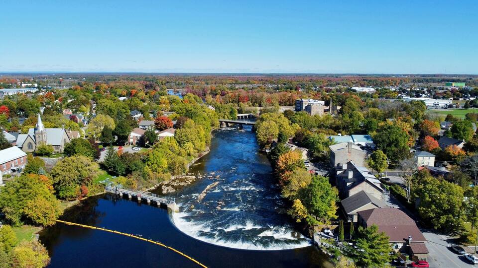 A river flowing through a town with autumn foliage, a bridge, and residential buildings.
