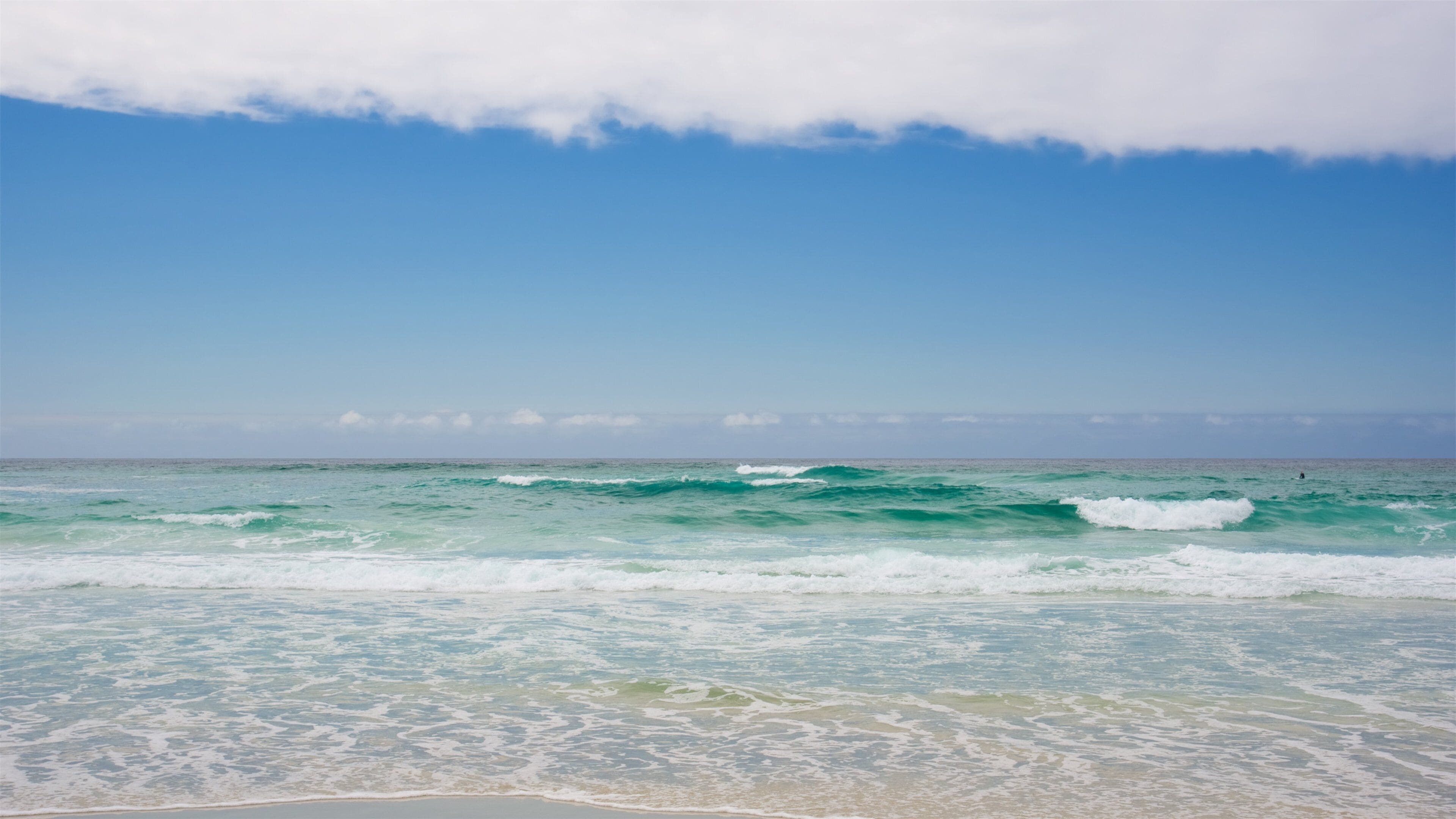 A beach with turquoise waves and a clear sky.
