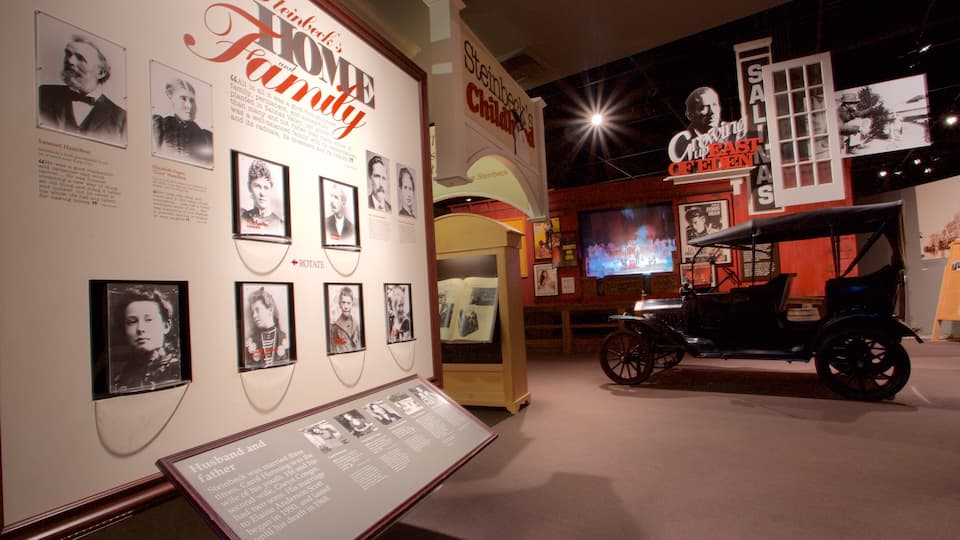 Una exposición de museo con fotografías enmarcadas, un coche antiguo y un cartel que dice 'Steinbeck's Home and Family'.
