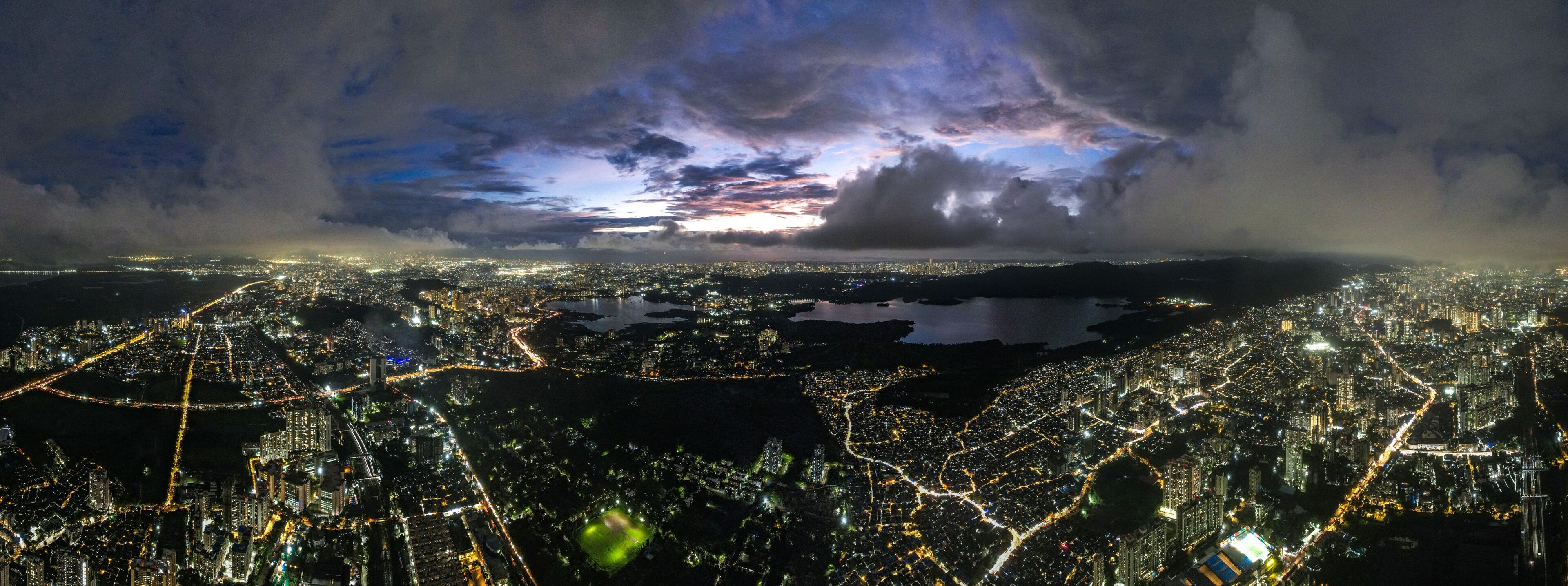 Aerial view of a sprawling cityscape with shimmering lights reflecting off Powai Lake under a dramatic twilight sky, Mumbai, Maharashtra, India.