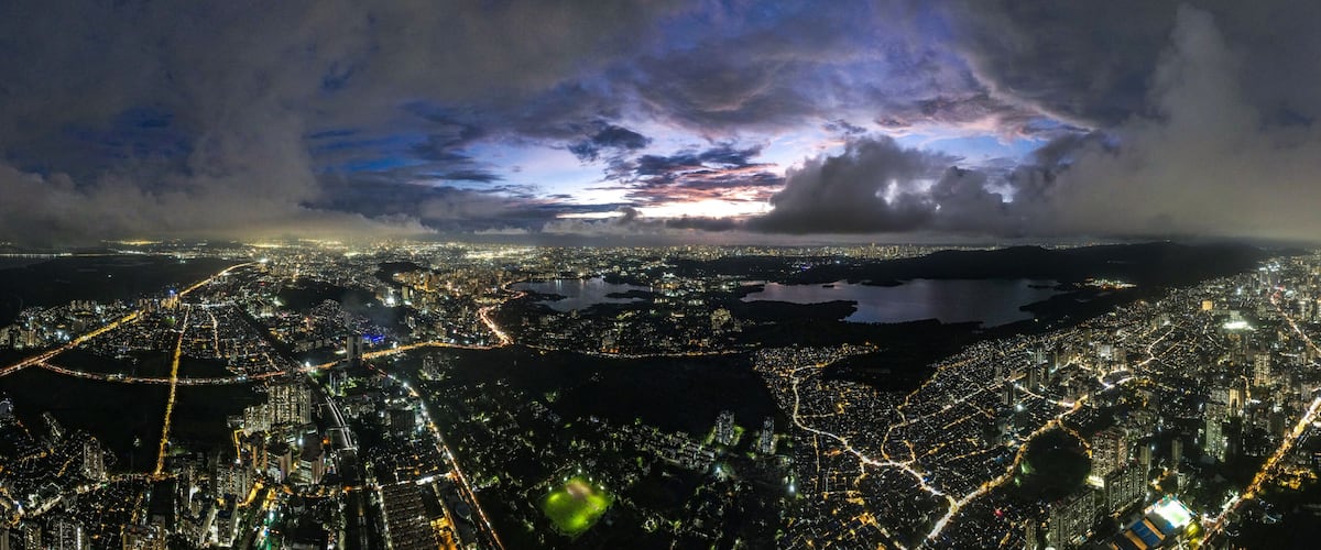 Aerial view of a sprawling cityscape with shimmering lights reflecting off Powai Lake under a dramatic twilight sky, Mumbai, Maharashtra, India.