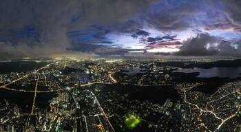 Aerial view of a sprawling cityscape with shimmering lights reflecting off Powai Lake under a dramatic twilight sky, Mumbai, Maharashtra, India.
