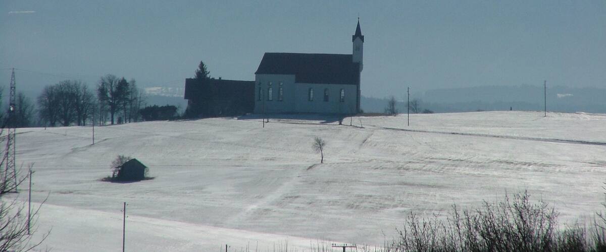 A church in a snowy field with mountains in the background.