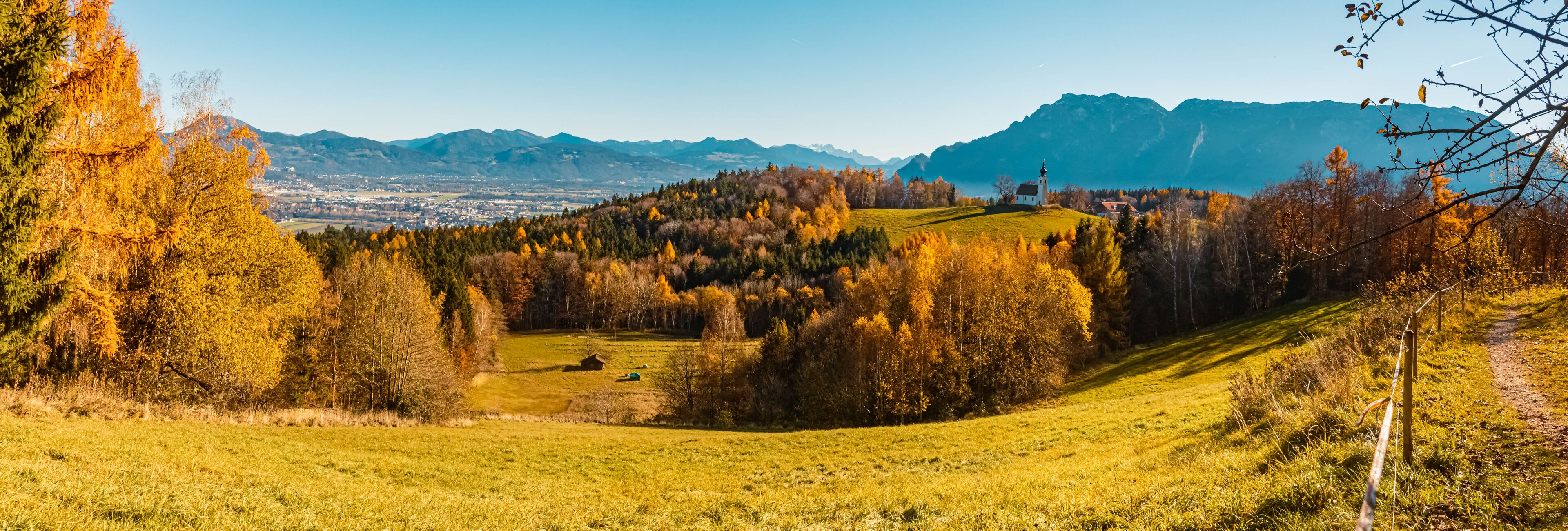 A hilly landscape with autumn-colored trees, a white church, and distant mountains.