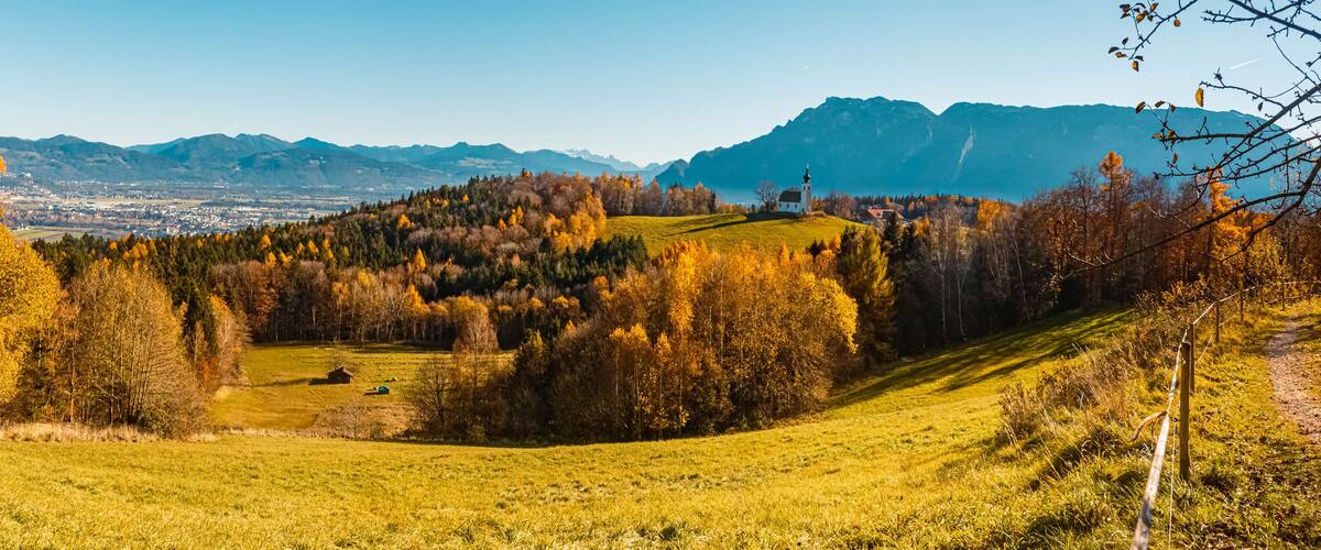 A hilly landscape with autumn-colored trees, a white church, and distant mountains.