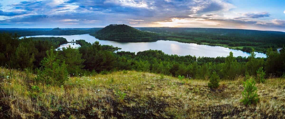 A lake surrounded by forested hills and a cloudy sky.