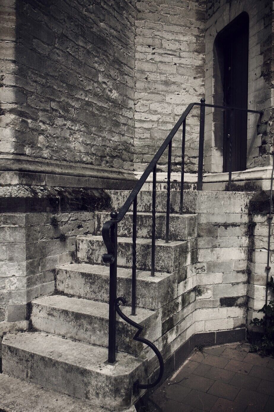 A set of stone steps with a metal railing leading to a dark doorway in a brick building.