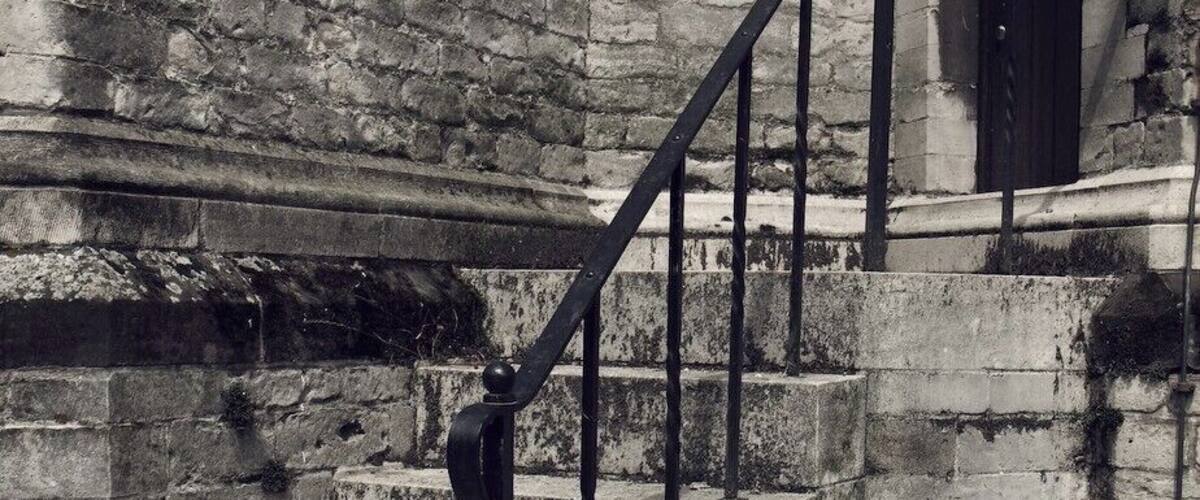 A set of stone steps with a metal railing leading to a dark doorway in a brick building.