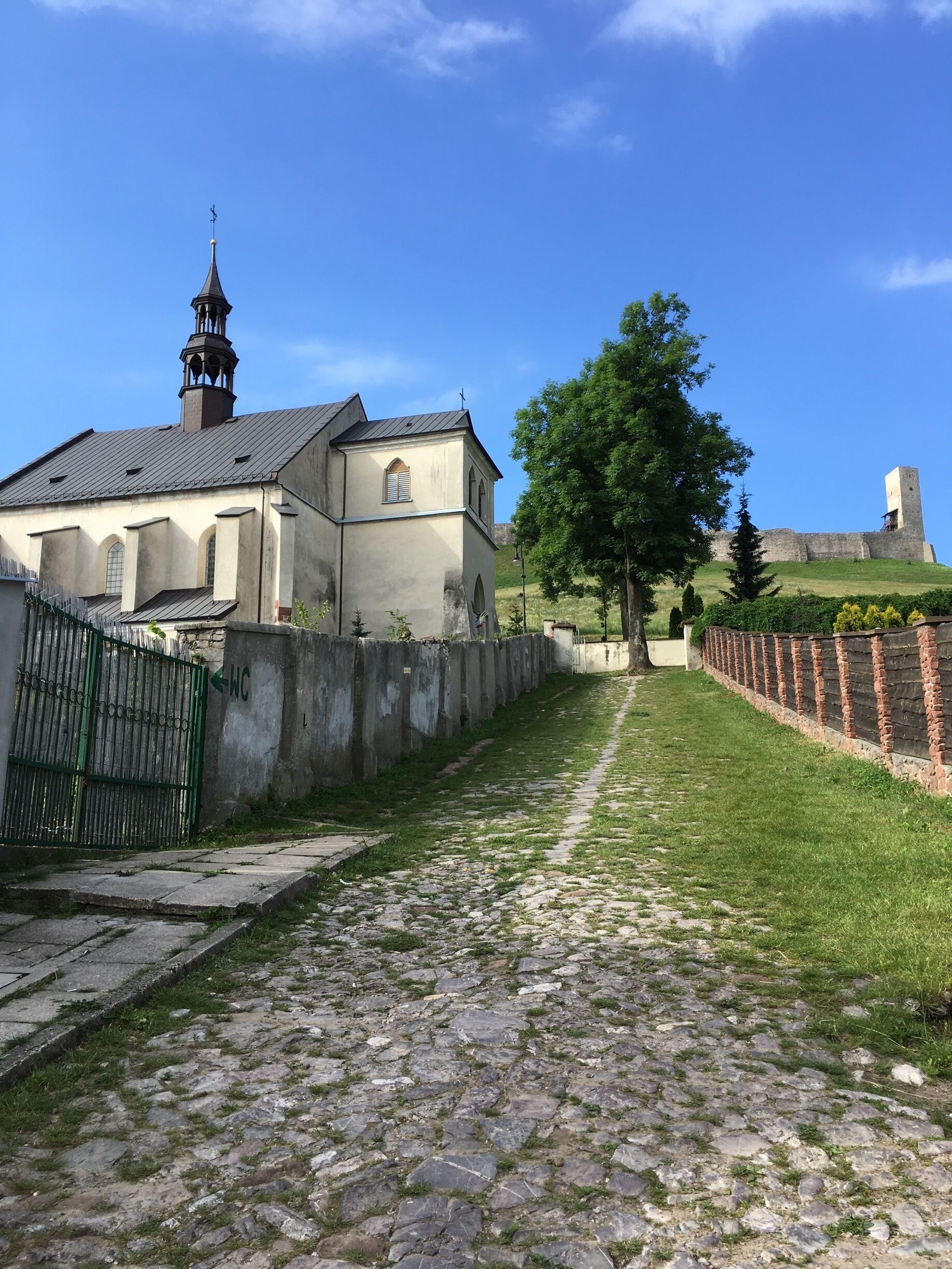 A church with a bell tower, a cobblestone path, and a castle in the background.