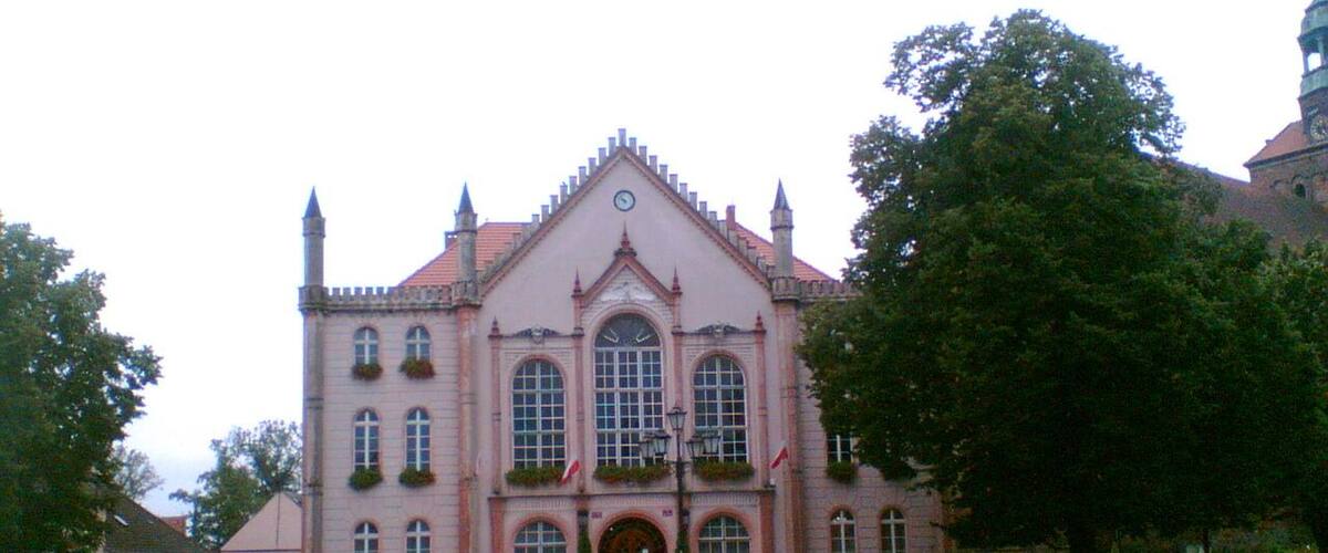 A pink building with arched windows and a clock, surrounded by cobblestone pavement and benches.