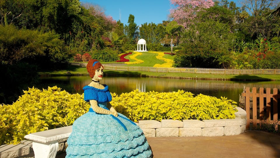 A LEGO sculpture of a woman in a blue dress by a pond with a gazebo in the background.