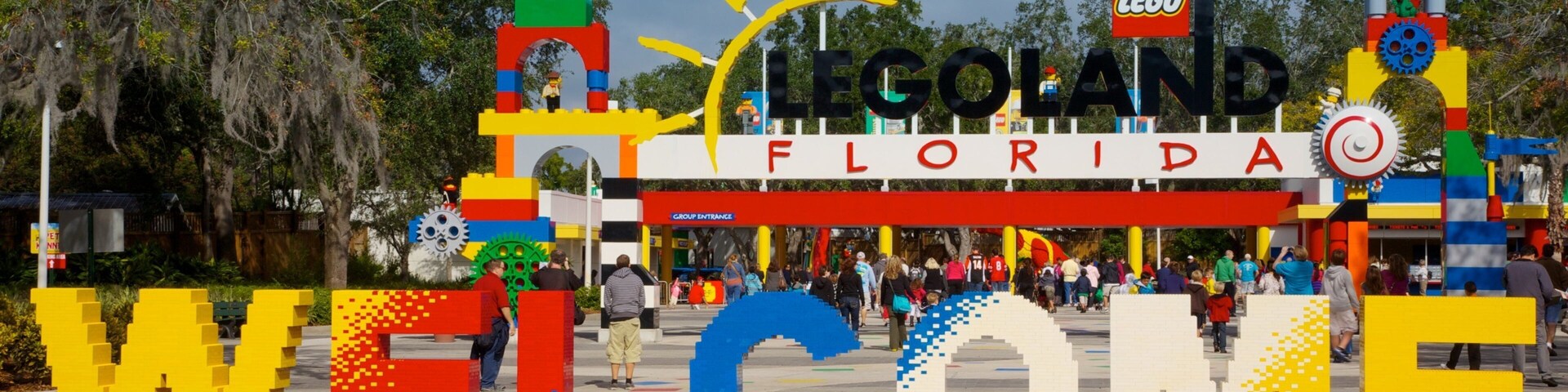 Un letrero de bienvenida con temática LEGO que dice 'LEGO FLORIDA' y 'BIENVENIDOS' en letras grandes, rodeado de follaje.