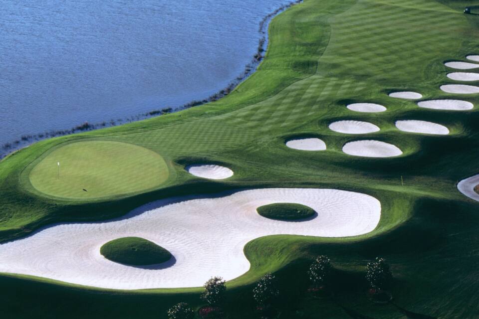 A golf course with sand bunkers and a body of water.