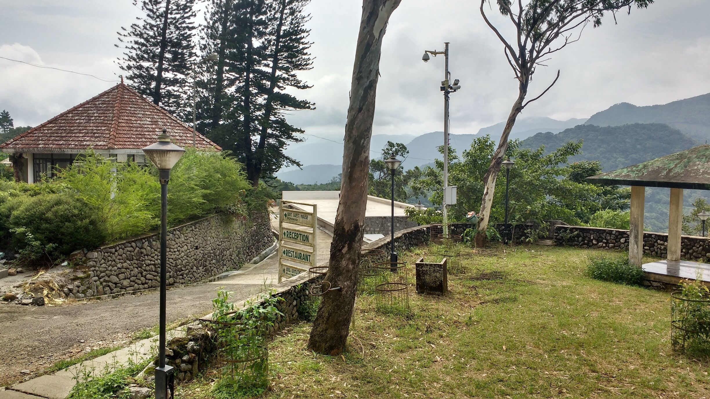 A stone wall, a guest house, and a reception sign in a lush, mountainous area.