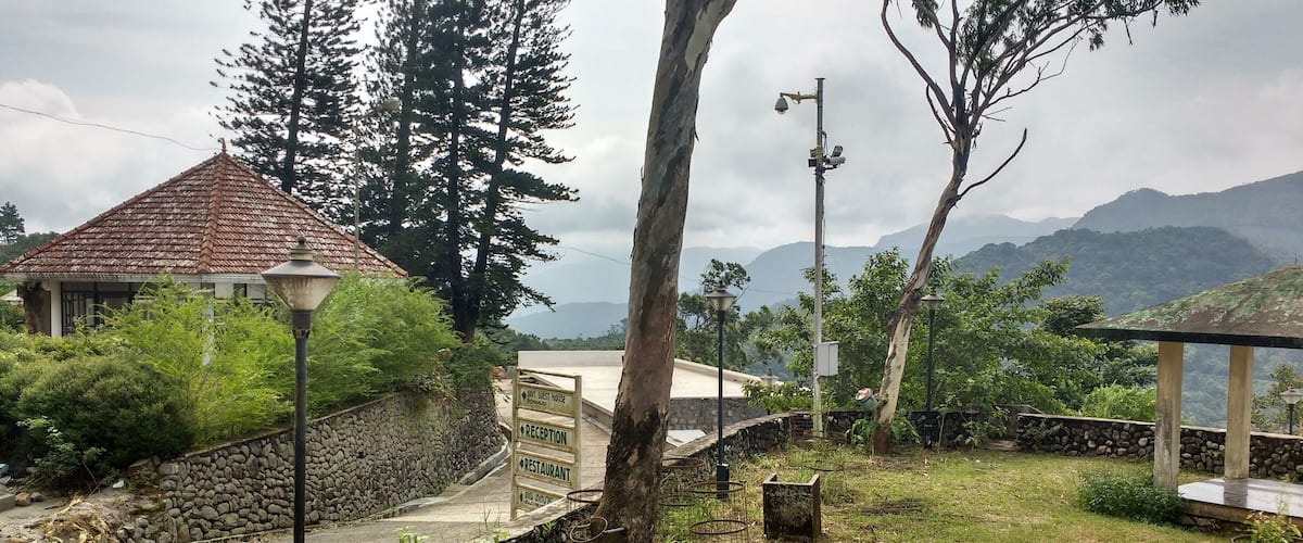 A stone wall, a guest house, and a reception sign in a lush, mountainous area.
