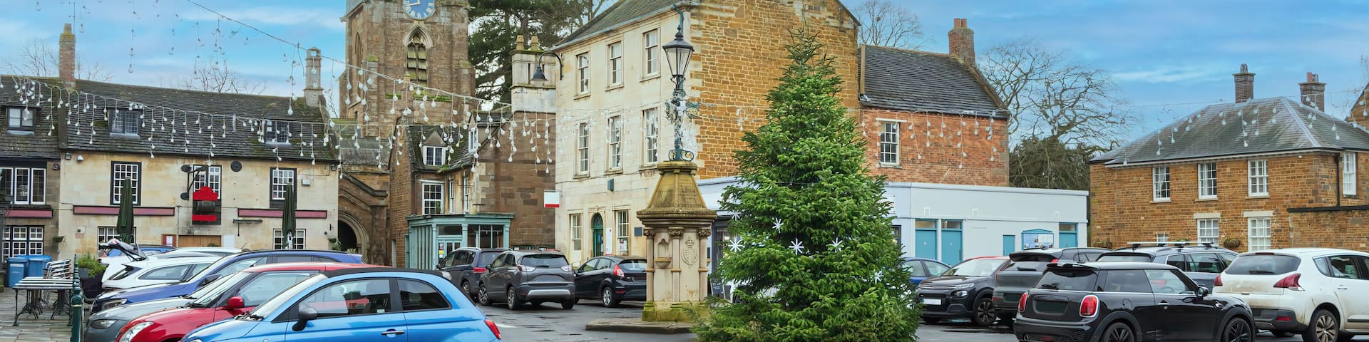 A town square with a church, parked cars, and a Christmas tree.