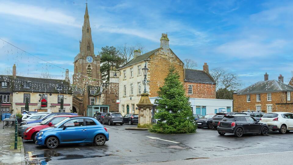 A town square with a church, parked cars, and a Christmas tree.