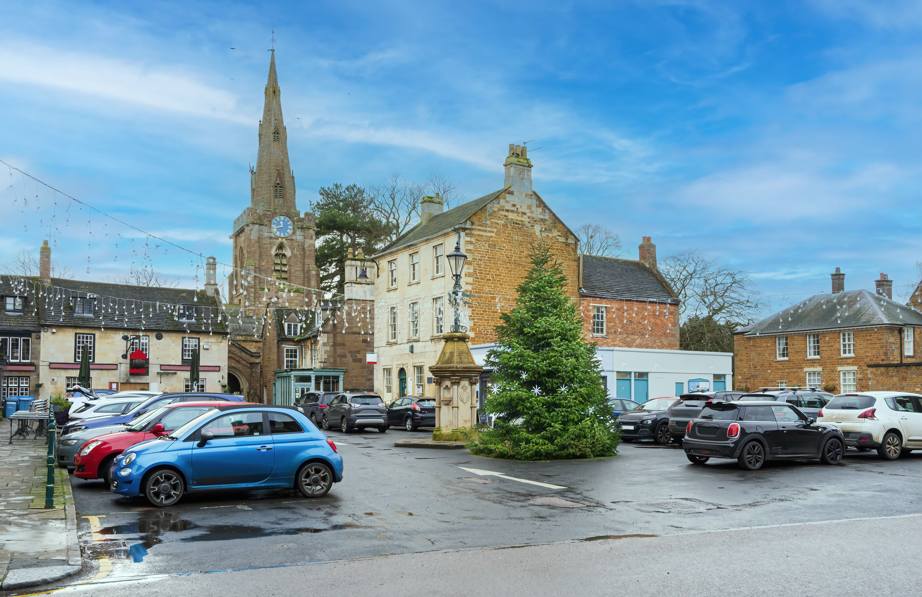 A town square with a church, parked cars, and a Christmas tree.