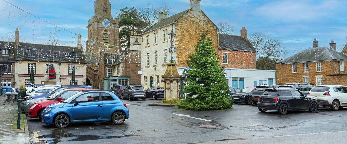 A town square with a church, parked cars, and a Christmas tree.