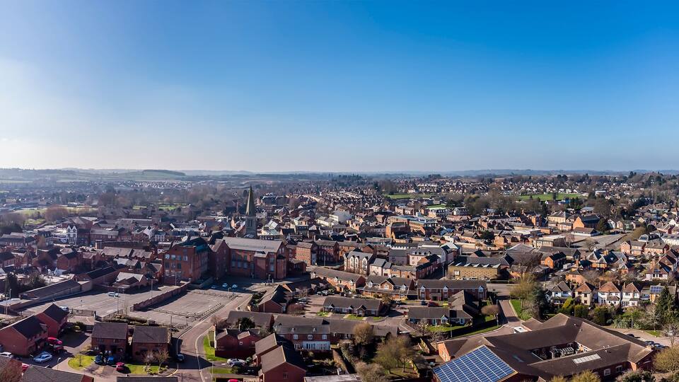 A panoramic view of a town with a prominent church steeple, residential houses, and a clear blue sky.