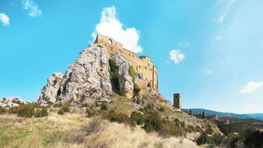 Un castillo de piedra histórico en una colina bajo un cielo azul despejado.