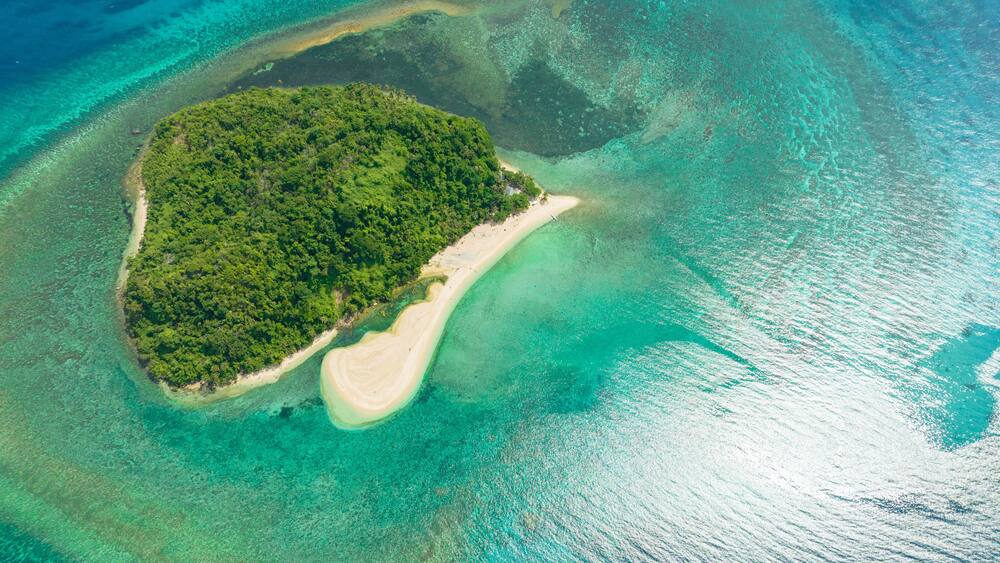 An aerial view of a small island with dense green vegetation and a sandy beach.