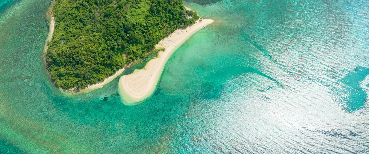 An aerial view of a small island with dense green vegetation and a sandy beach.