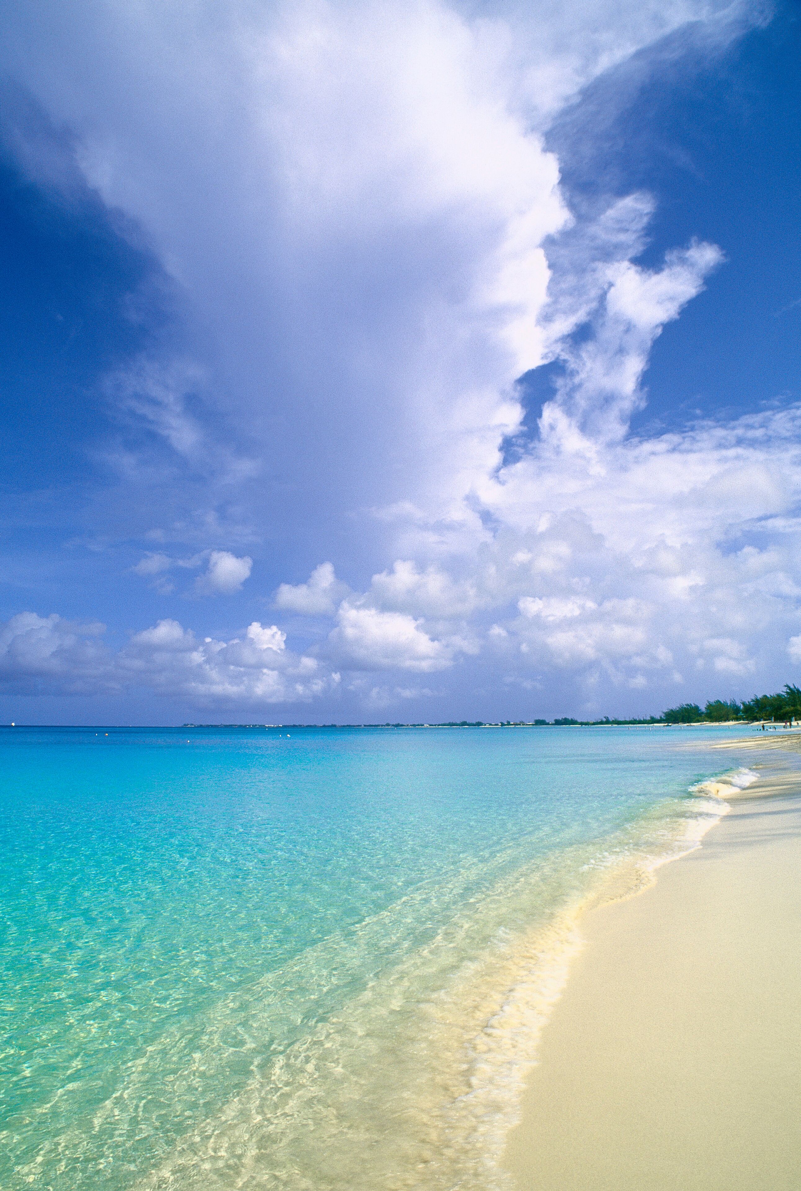 A beach with clear turquoise water, a sandy shore, and a partly cloudy sky.