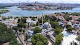 Une vue urbaine mettant en valeur une mosquée imposante, dotée de plusieurs dômes et d’un minaret élevé, le tout entouré d’arbres verdoyants et traversé par une rivière.