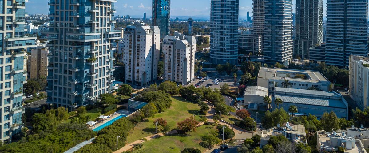 A cityscape with modern high-rise buildings, a clear blue sky, and a park area with a swimming pool.