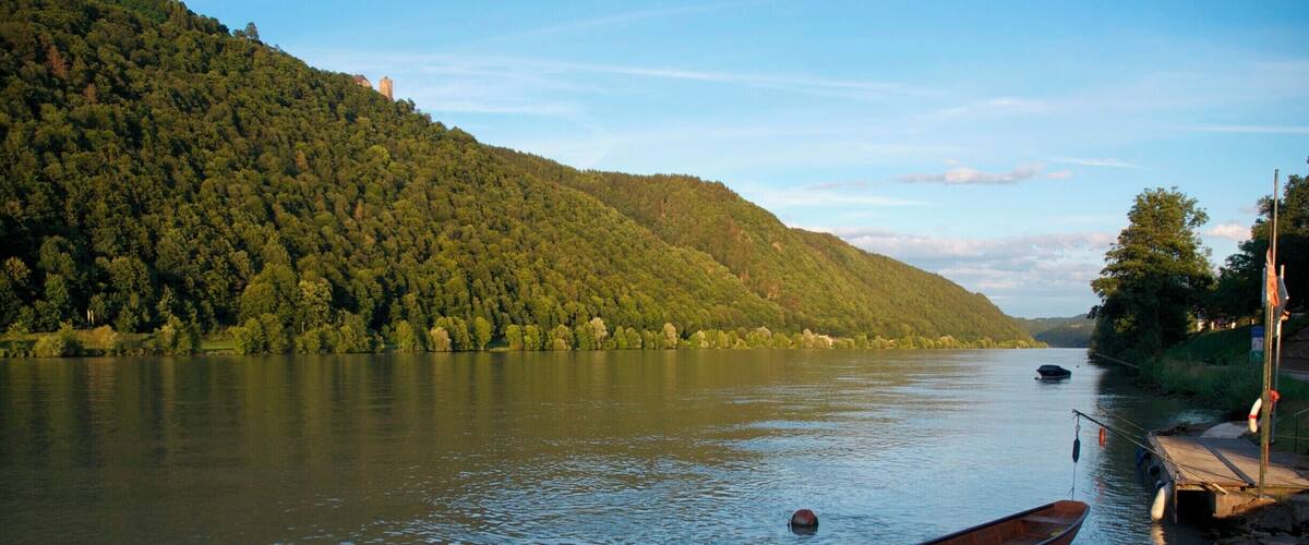 A calm river with a wooden boat tied to a dock, surrounded by lush green hills.