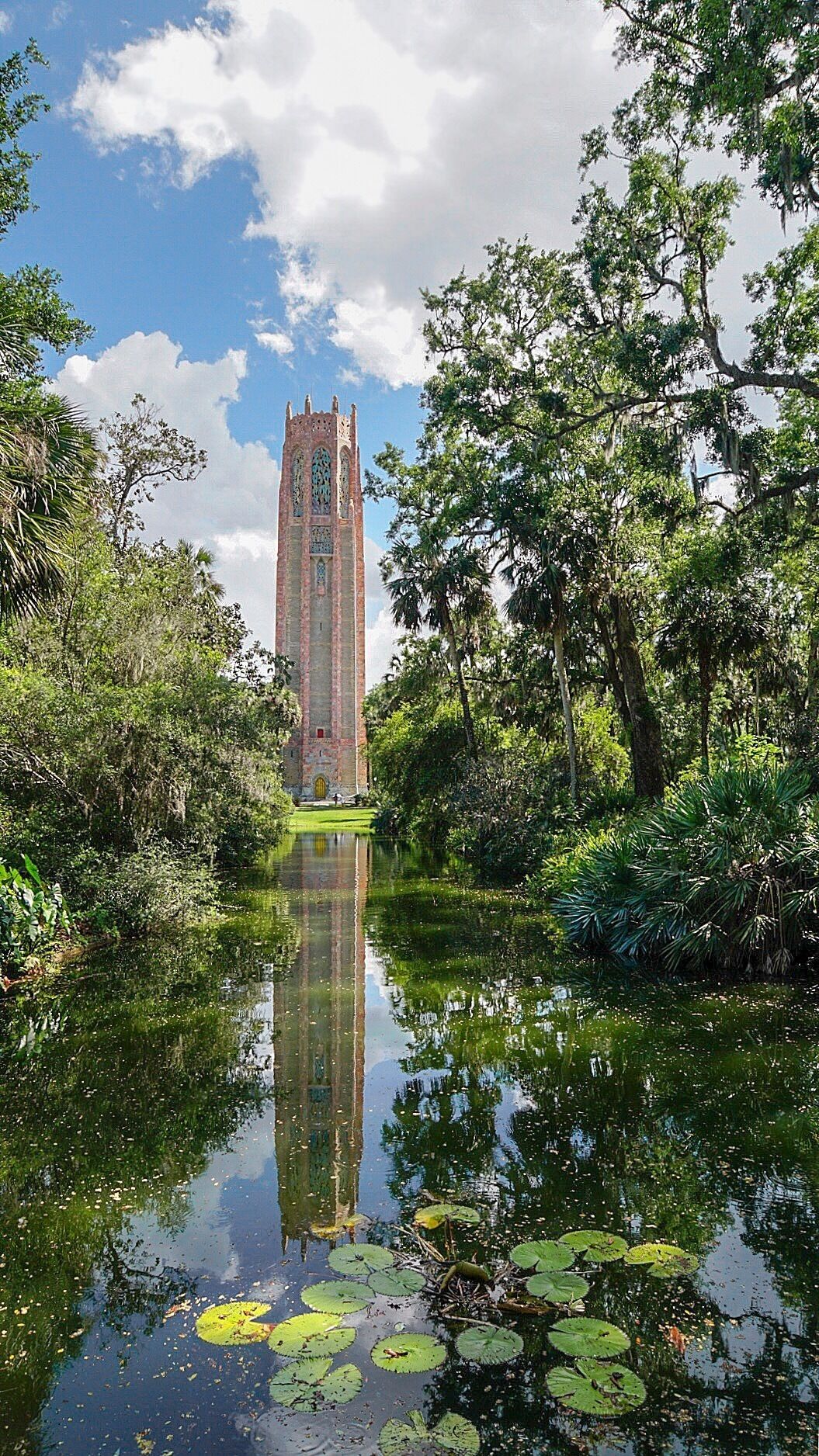 A tall brick tower surrounded by lush greenery and a calm pond with lily pads.