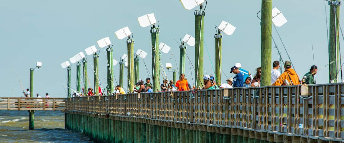 A pier with people fishing, wooden posts, and a wooden walkway.