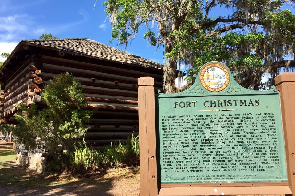 A historical marker for Fort Christmas, a wooden structure surrounded by trees and greenery.