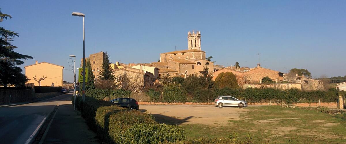 A historic building with a tower, surrounded by greenery and parked cars.