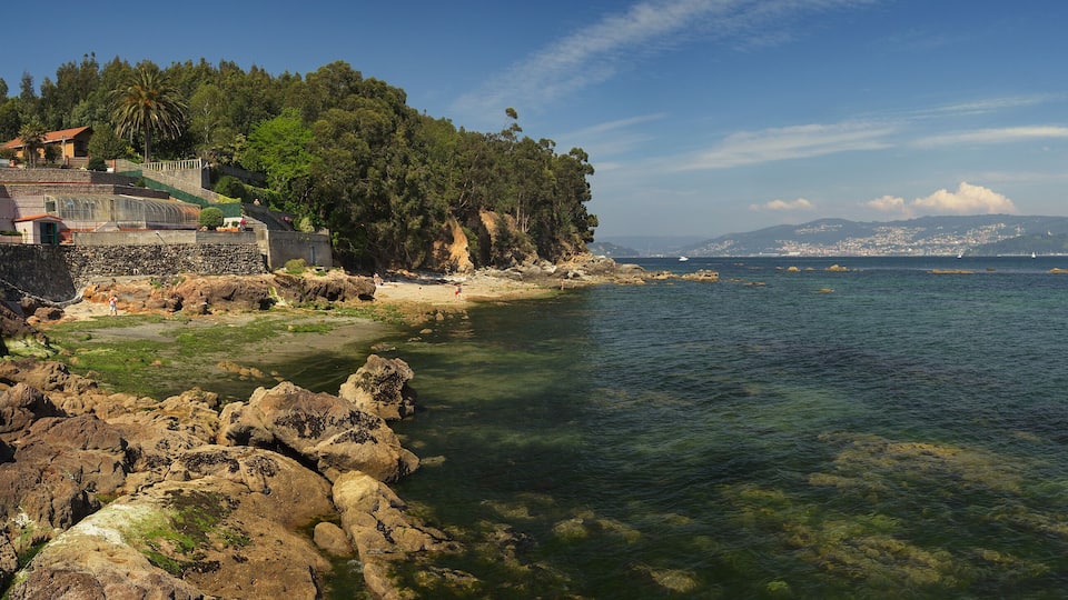 A coastal landscape with rocky shores, clear water, and a city in the distance.