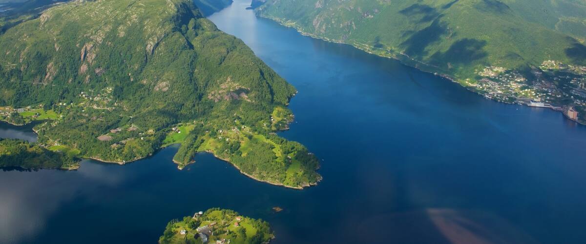 A mountainous landscape with a large body of water, green hills, and a small settlement near the water's edge.