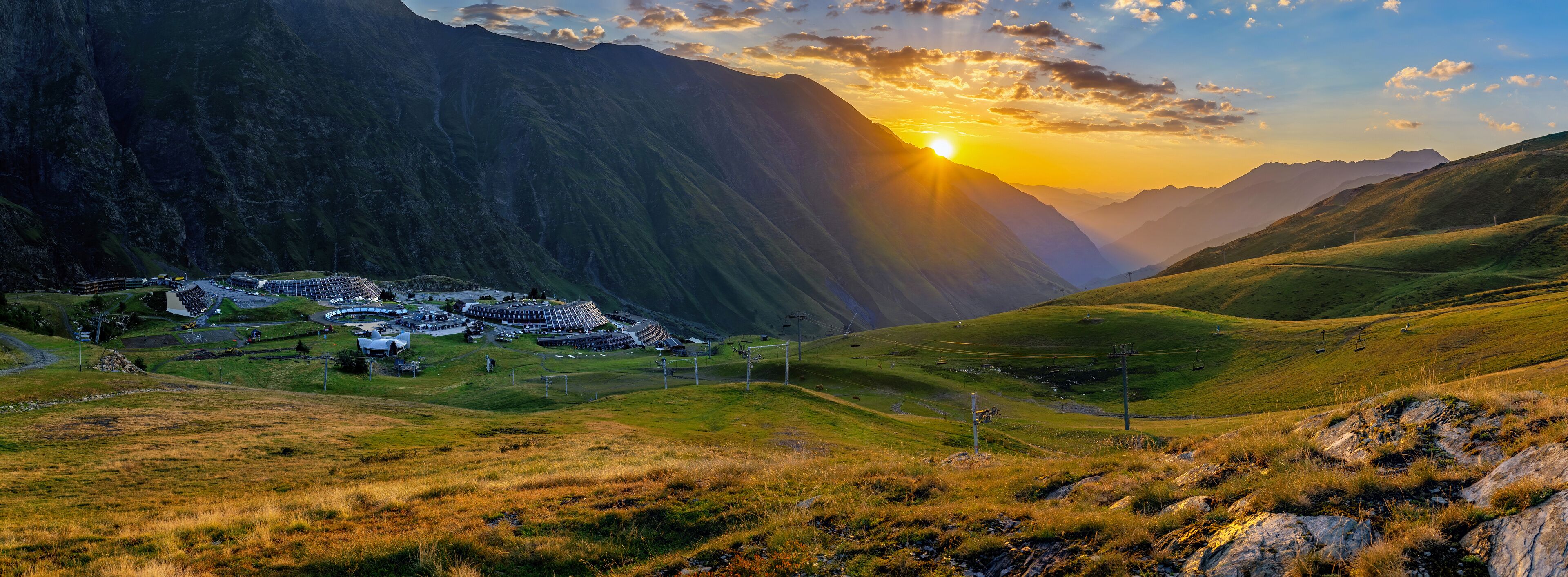 A mountainous landscape with a village nestled in a valley, surrounded by steep cliffs and a sunset.