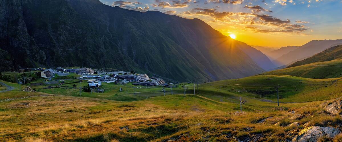 A mountainous landscape with a village nestled in a valley, surrounded by steep cliffs and a sunset.