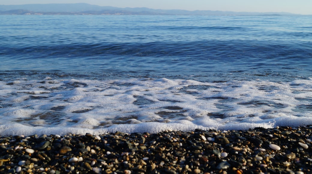 A pebbly beach with calm sea waves and distant mountains.