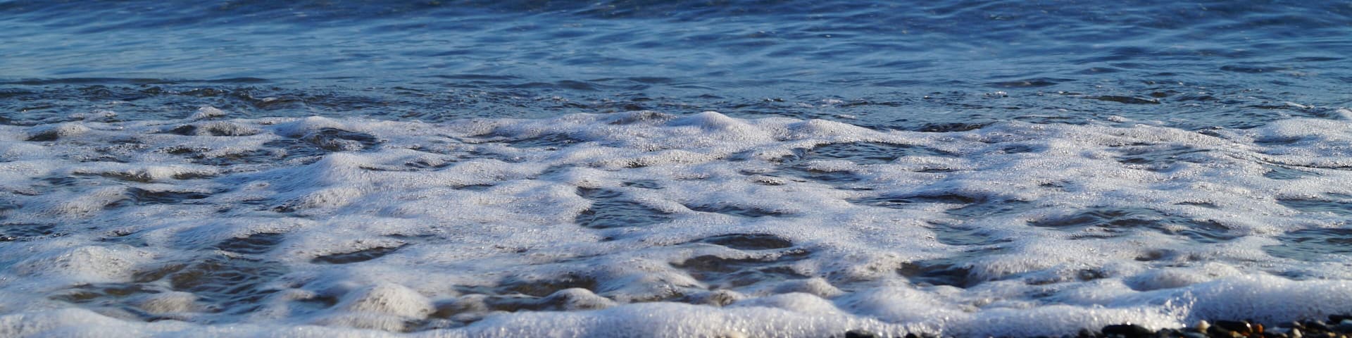 A pebbly beach with calm sea waves and distant mountains.
