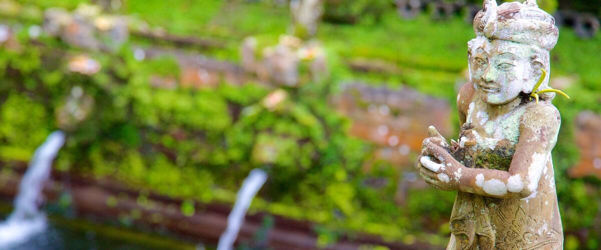 A statue of a figure holding a plant, with a fountain in the background.