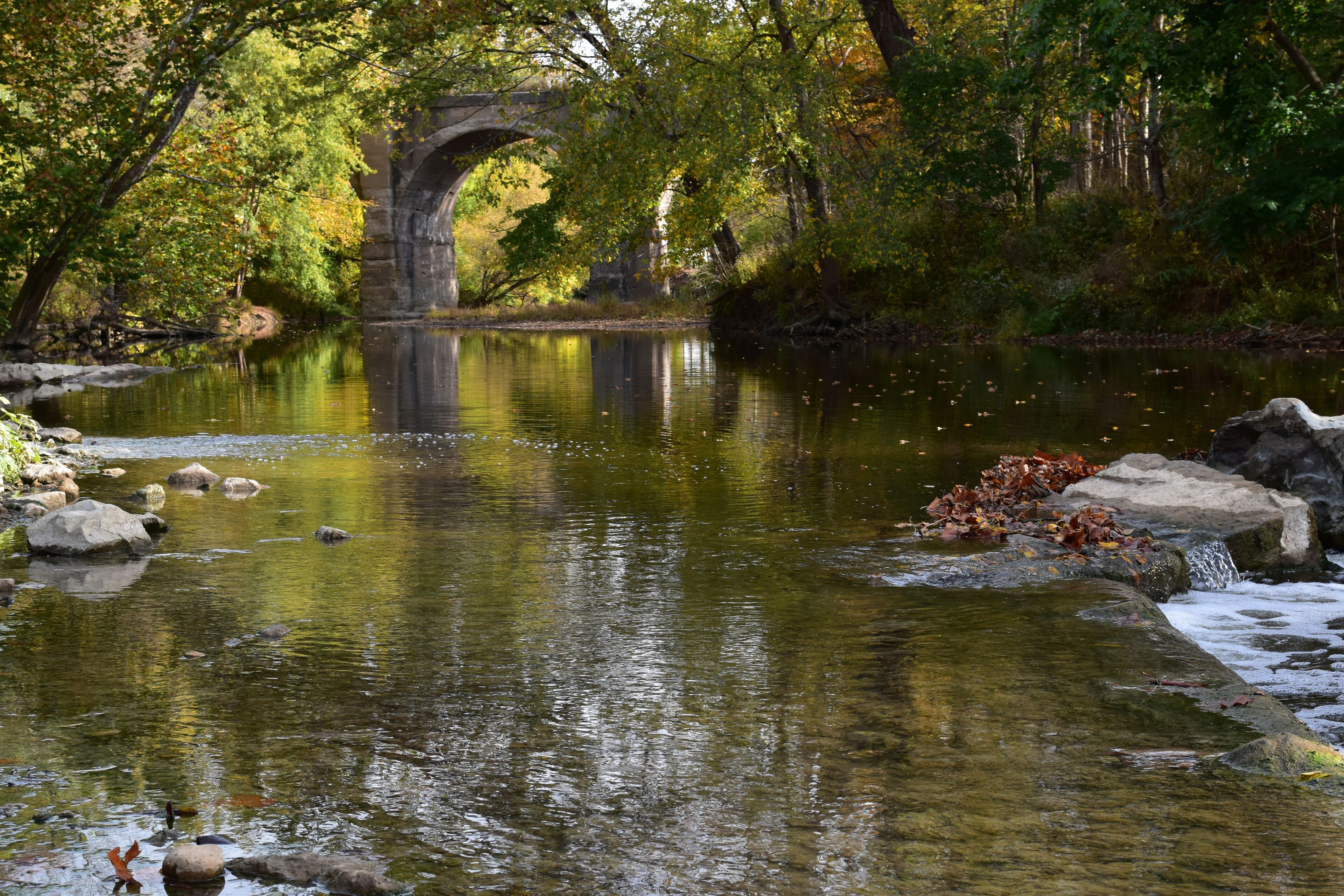 Eagle creek runs through a park in Indiana with an old, usused, arched bridge visible in the background